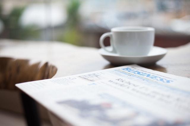 the business section of a aper on a table next to a cup of coffee
